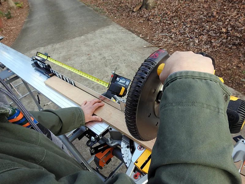 worker uses miter saw with measuring system to cut board